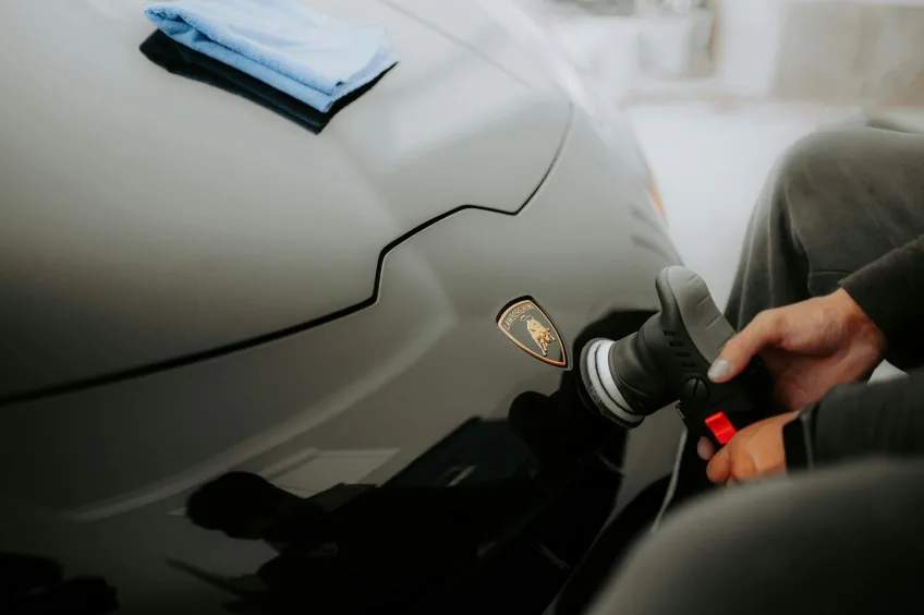 Technician machine-polishing a black Lamborghini hood during paint correction before ceramic coating