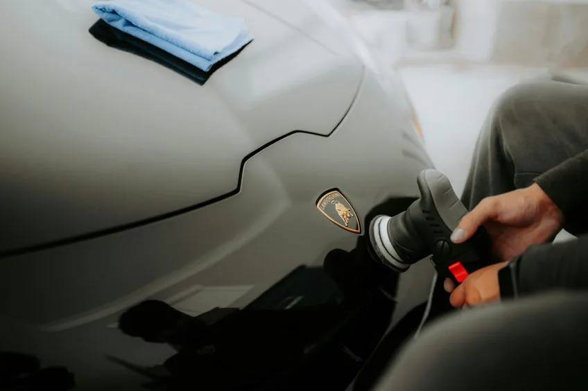 Technician machine-polishing a black Lamborghini hood during paint correction before ceramic coating