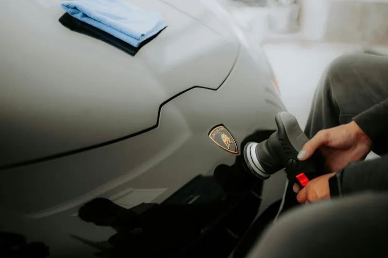 Technician machine-polishing a black Lamborghini hood during paint correction before ceramic coating