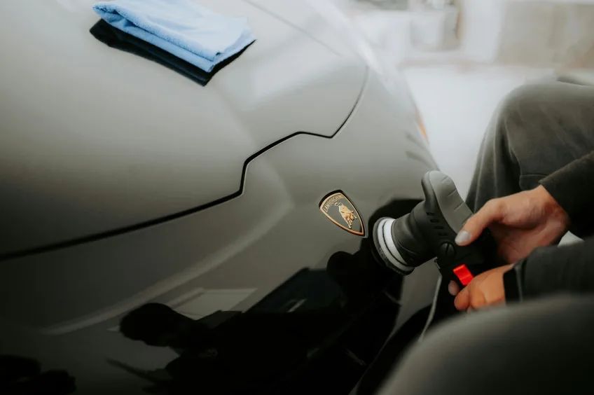 Technician machine-polishing a black Lamborghini hood during paint correction before ceramic coating