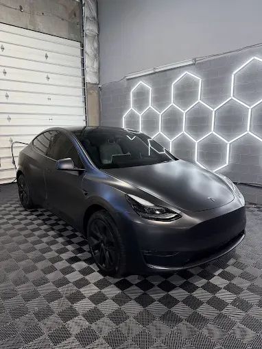 Matte charcoal Tesla with paint protection under hexagonal shop lights in Chantilly